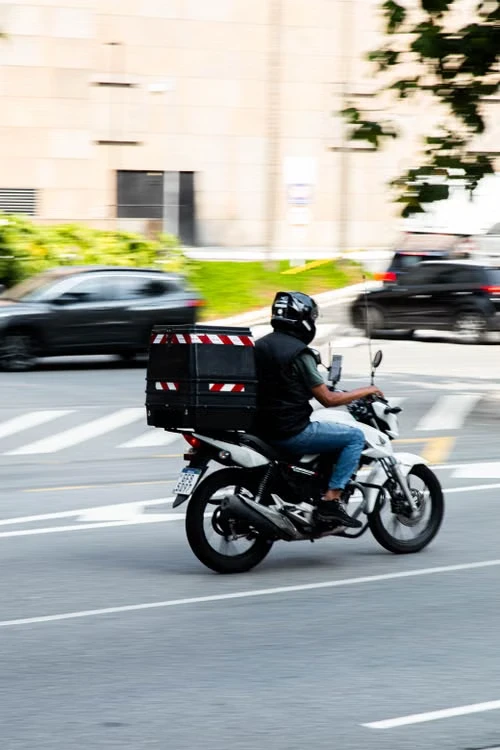 Repartidor en moto con caja de delivery en la vía